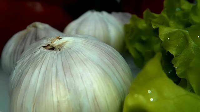 The camera moves slowly next to the rows of ripe garlic bulbs and appetizing green salad leaves, as well as the fruits of sweet bell pepper. Macro. Closeup. Shallow depth of field. Ultra small special