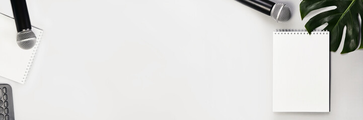 Podcast concept. White notebook with blank sheet. Black microphone and green monstera leaf....