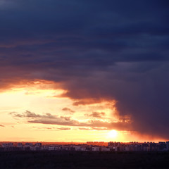 Obraz premium Cloudy sky over the houses during the orange sunset