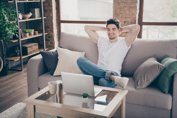 Portrait of his he nice attractive muscular cheerful cheery guy sitting on divan resting working remotely part-time at modern industrial loft interior style living-room indoors