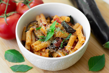 Traditional Italian dish: pasta alla norma with tomatoes, eggplant, garlic, basil and ricotta cheese on a wooden cutting board