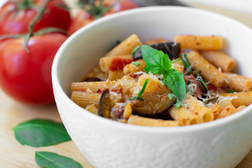 Traditional Italian dish: pasta alla norma with tomatoes, eggplant, garlic, basil and ricotta cheese on a wooden cutting board