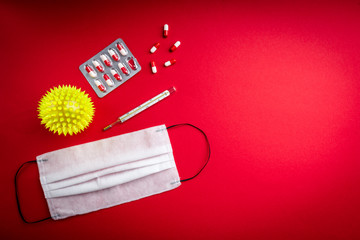 Yellow ball, pills, thermometer and medical mask on red background. Coronavirus disease COVID-19.