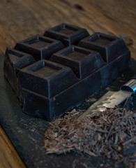 Dark chocolate bar on the black slate with steal knife.