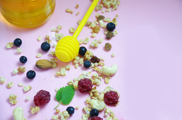 jar of honey with spoon for honey. Healthy breakfast ingredients. berries, granola, oatmeal, almonds, cashews, blueberries, raspberries healthy eating, keto diet, fitness nutrition top view, on pink