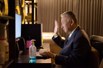 Mature Japanese businessman video calling while working overtime at home late at night