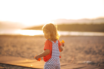  a little girl with blond hair walks along the beach and looks at the sea, the setting sun