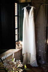 A beautiful white wedding dress. Wedding dress hanging near the window.