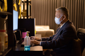 Mature Japanese businessman with mask working overtime at home late at night