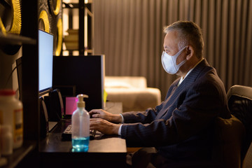 Mature Japanese businessman with mask working overtime at home late at night