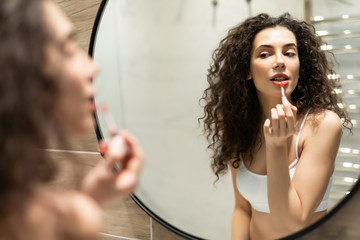 Everyday makeup. Young woman applying lipstick on Lips in front of mirror in bathroom.