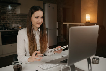 Remote work. A brunette woman with headphones working remotely online on her laptop. A girl discussing problems with her colleagues during an online business briefing at her cozy home workplace.