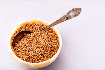 Raw dry buckwheat grain in a bowl with a spoon close-up.