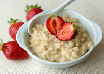 
Oatmeal with strawberries in a white bowl. Healthy breakfast with oatmeal and fresh organic berries. Hot and healthy breakfast. Dietary nutrition. Top view, close up