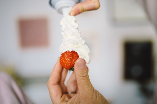 main qui tient une fraise avec de la chantilly 