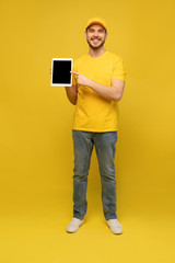 Cool delivery man with tablet. demonstrates tablet. looking at camera. isolated on yellow background.