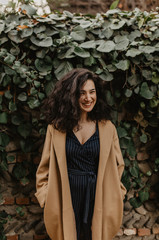 Fototapeta premium Beautiful girl with black curly hair standing and smiling near the bush