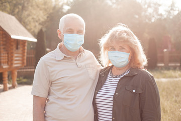 Happy elderly seniors couple wearing medical mask to protect from coronavirus in summer park, coronavirus quarantine