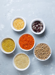 Rice, bulgur, beans, peas, lentils and chickpeas in white bowls on a gray background. Cereals are a source of energy. Healthy food concept. Top view.