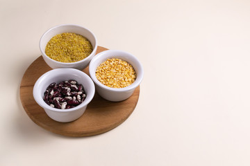Bulgur, beans, peas in white bowls on a wooden cutting board on a light yellow background. Healthy food concept. Horizontal orientation. Top view. Copy space.