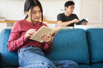 Obraz premium Photo of young concentrated asian couple reading books while sitting