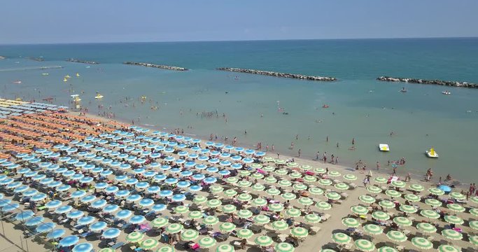 Aerial view of colored umbrellas lined up in Riccione beach. People on the beach sunbathe or shade in the shade before a bath at sea.