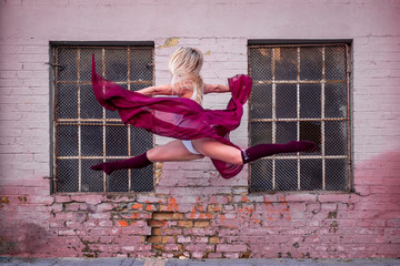 Beautiful young woman make performance on stret, she jump in front of window in old part of town