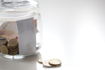Jar of glass with metal coins and paprer money on white table save for future