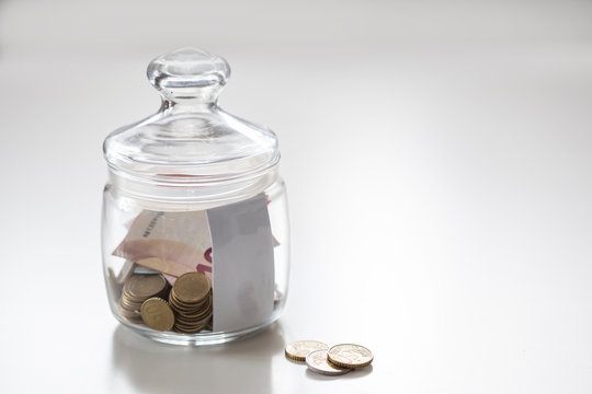 Jar of glass with metal coins and paprer money on white table save for future