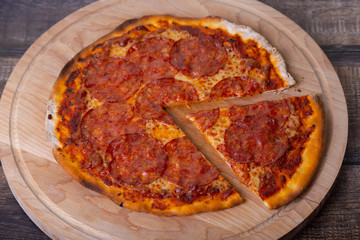 Pizza with chorizo sausage on a wooden board. Whole pizza, one piece cut off. Close-up.