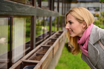 Horizontal portrait in profile of a caucasian blonde woman in coat. A model stands outdoors against the background of a wall of a building in the city.