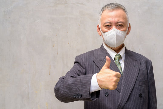 Mature Japanese Businessman With Mask Giving Thumbs Up Outdoors