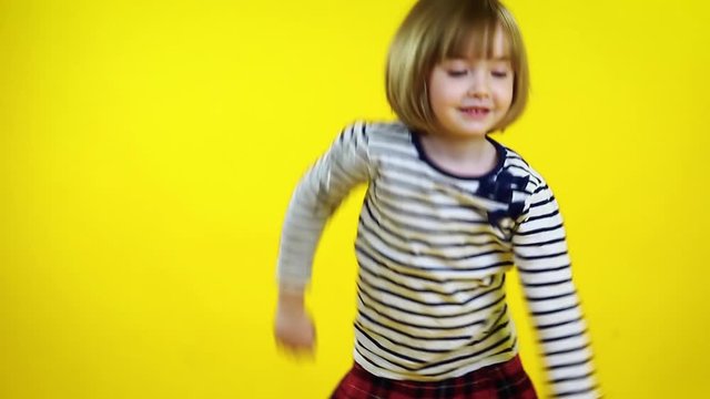 Happy little girl in red hat dancing over yellow background. Cute blonde child.