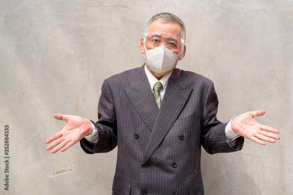 Poster Mature Japanese businessman with mask and face shield shrugging shoulders