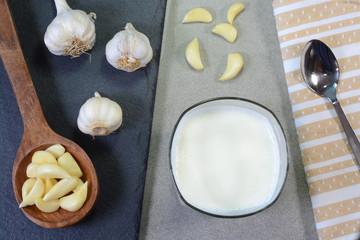 Hot garlic milk in a glass cup with peeled garlic on the background