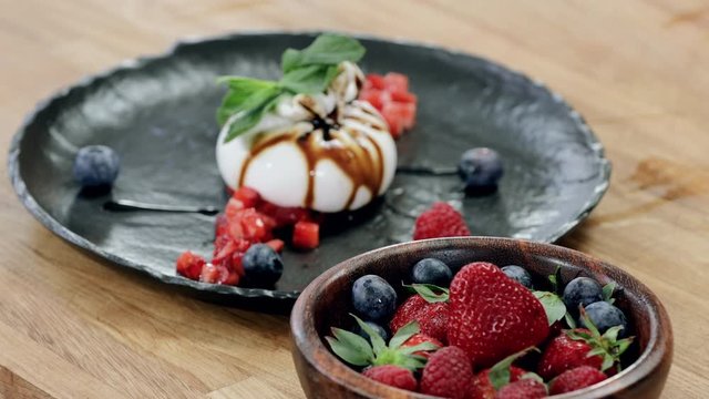 Delicious dessert for breakfast. Buratta cheese and fresh berries: strawberries, blueberries, raspberries and mint leaf on a plate served in the restaurant. 4K