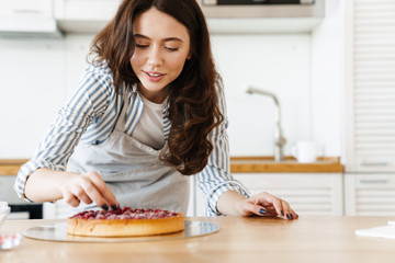 Image of pleased beautiful woman cooking pie with raspberries