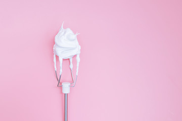 Whipped egg whites on mixer whisk on a pink background