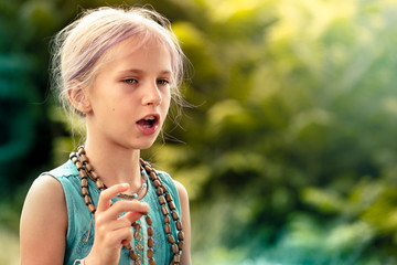 a cute teen girl with blonde hair chants a mantra on a rosary. Yoga, spirituality concept.
