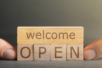 welcome open  inscription engraved on blocks that hold fingers on a gray background