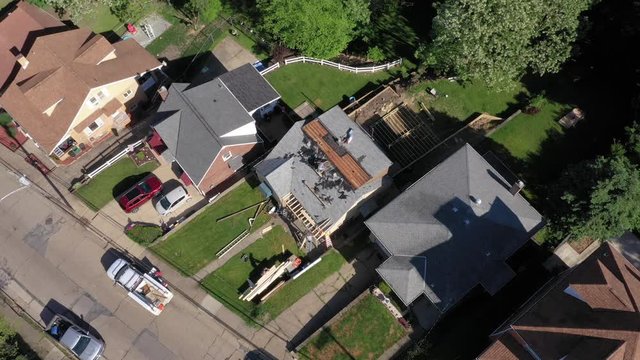 A high orbiting aerial flyover of roofers removing the shingles of a house before laying down a new roof. Pittsburgh suburbs.  	