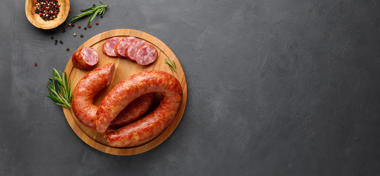 Smoked sausage with rosemary on a black slate background. Top view. Flat lay. Copy space for text.