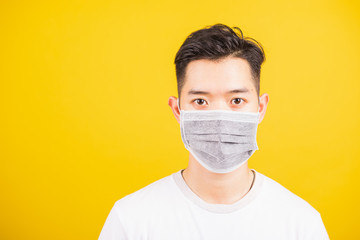Closeup Asian young man wearing face mask protective germ virus or air dust, studio shot isolated on yellow background and copy space, medical outbreak coronavirus COVID-19 concept
