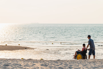 Asian special child in wheelchair and Father on the beach with overflowing light of the sunset, They are happiness in holidays with the travel,Life in the education age and happy disabled kid concept.