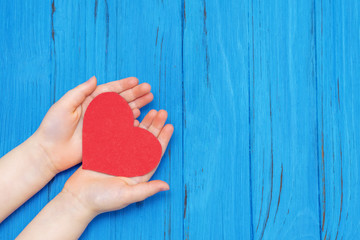 Top view of red heart in hands of child on a blue wooden background. Copy space.