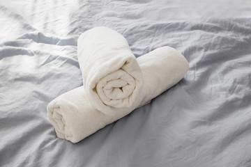 Rolled white clean towels on the bed with grey bedlinen.