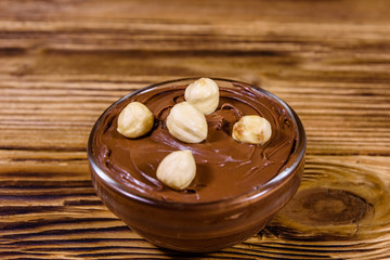 Glass bowl with chocolate spread and hazelnuts on a wooden table