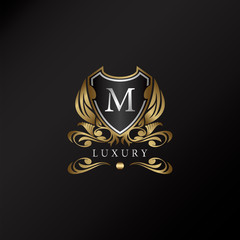 Shield logo in gold color with letter M Logo. Elegant logo vector template made of wide silver alphabet font on shield frame ornate style.
