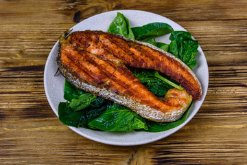 Plate with roasted salmon steak and spinach leaves on a wooden table