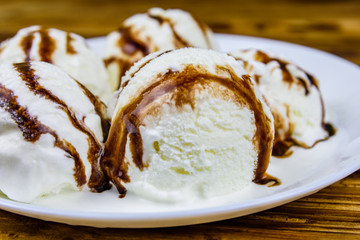 Plate with ice cream balls and chocolate topping on a wooden table